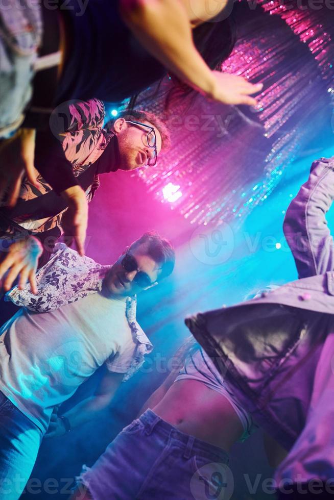 View from below of young people that having fun in night club with colorful laser lights photo