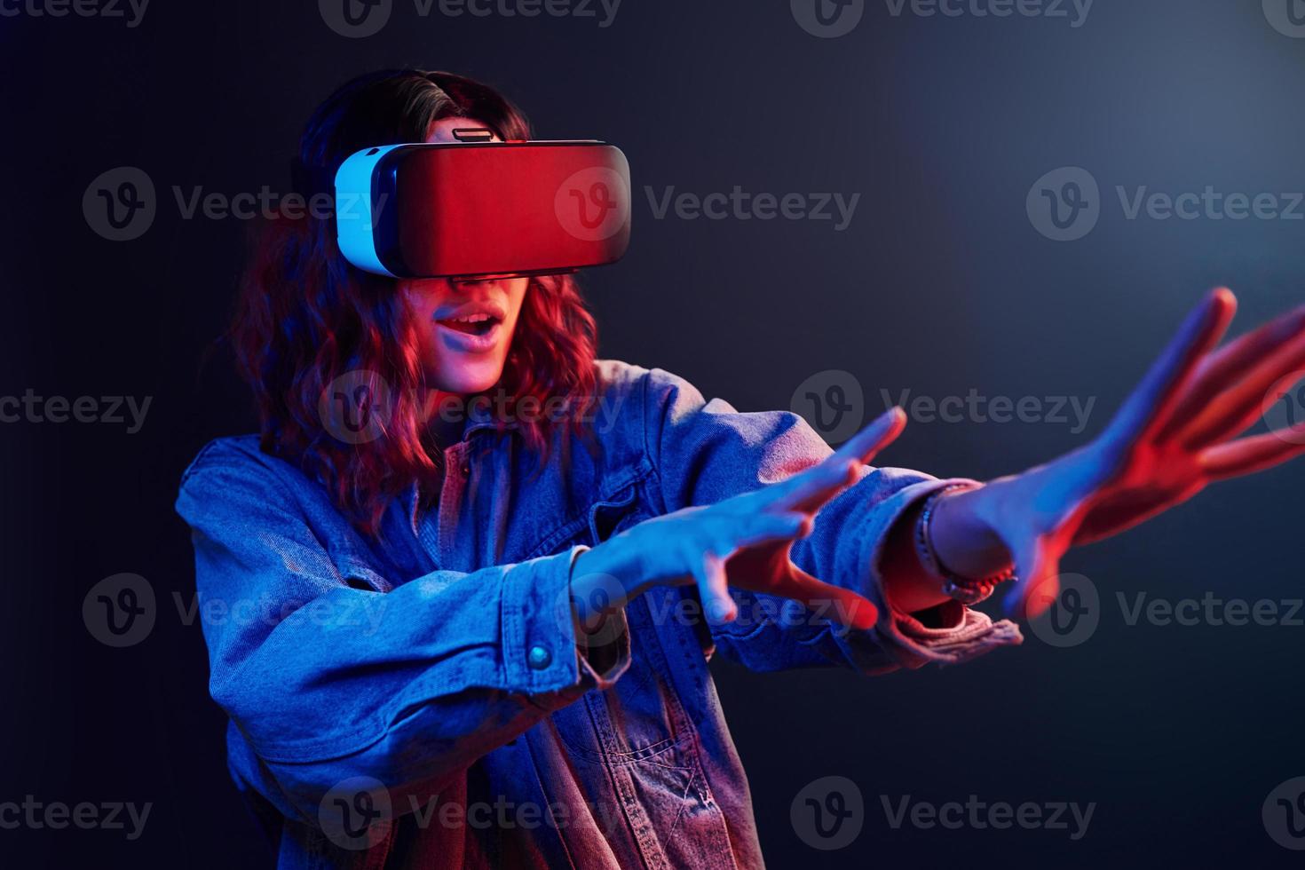 expresión facial de una joven con gafas de realidad virtual en la cabeza en neón rojo y azul en el estudio foto