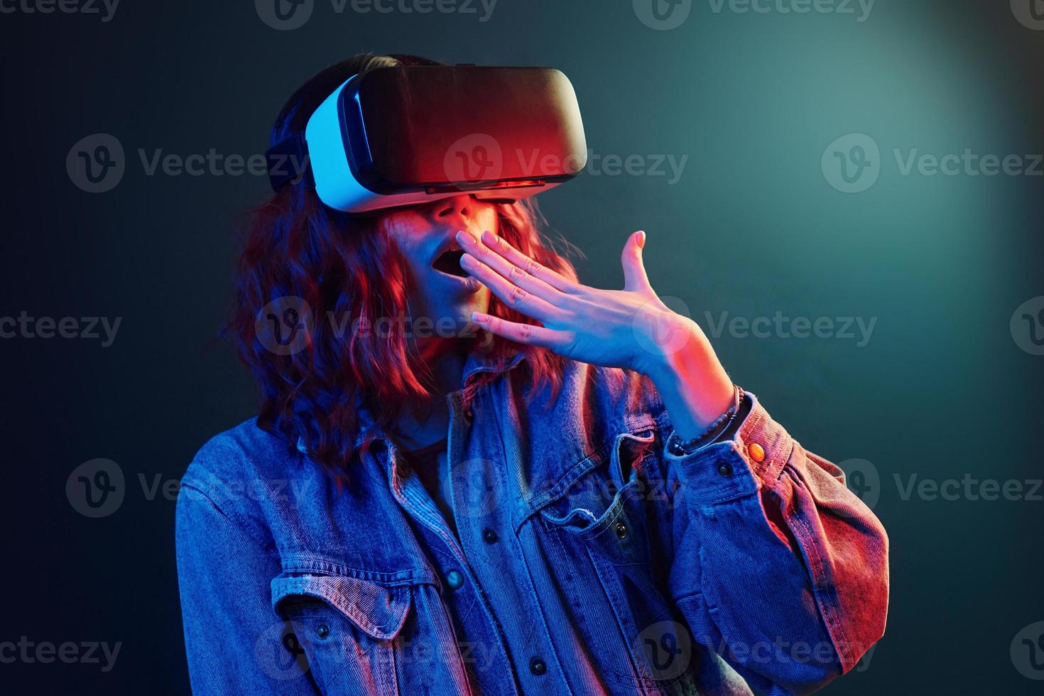 Facial expression of young girl with virtual reality glasses on head in red and blue neon in studio photo