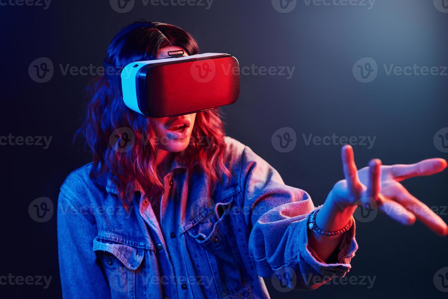 expresión facial de una joven con gafas de realidad virtual en la cabeza en neón rojo y azul en el estudio foto