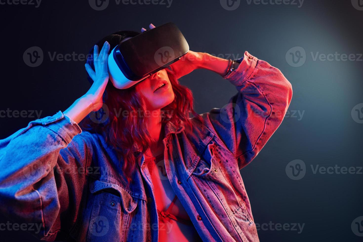 expresión facial de una joven con gafas de realidad virtual en la cabeza en neón rojo y azul en el estudio foto