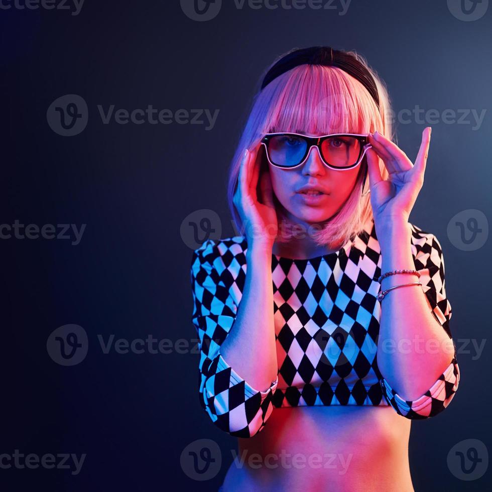 Portrait of young girl with blond hair in eyeglasses in red and blue neon in studio photo