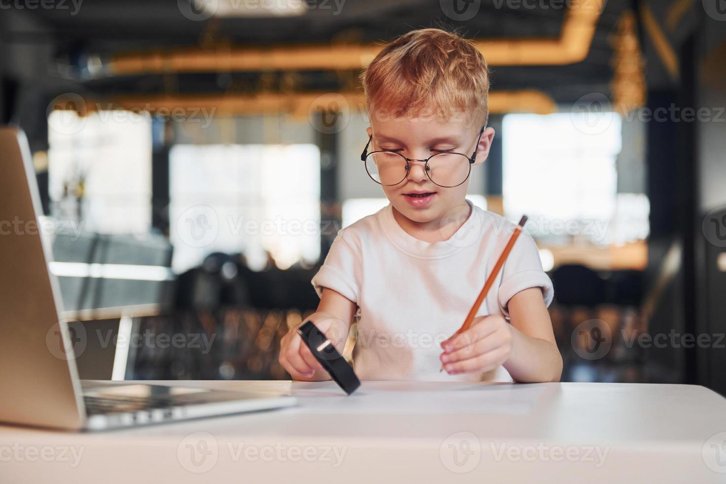 Smart child in casual clothes with laptop on table have fun with magnifying glass photo