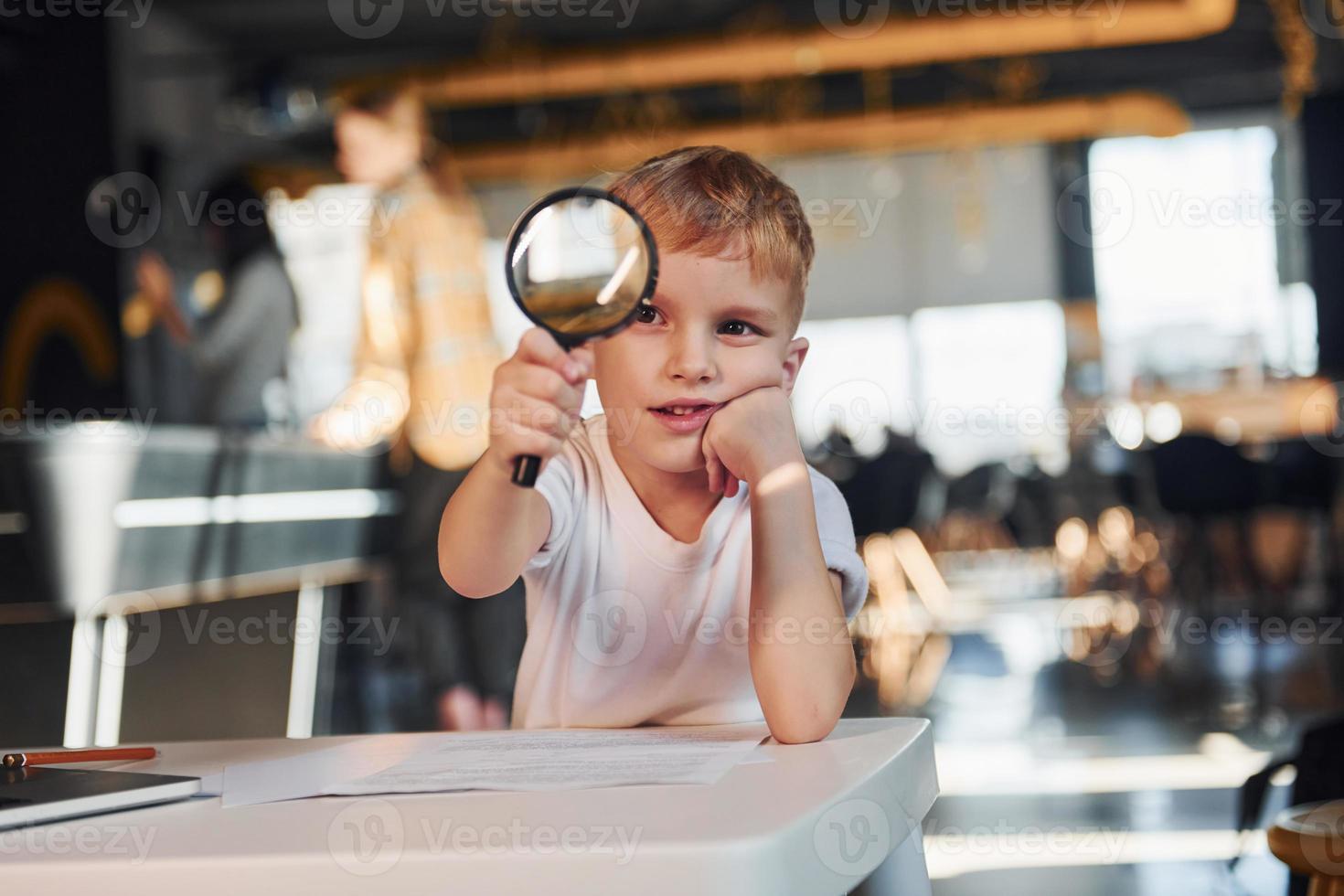 Smart child in casual clothes with laptop on table have fun with magnifying glass photo