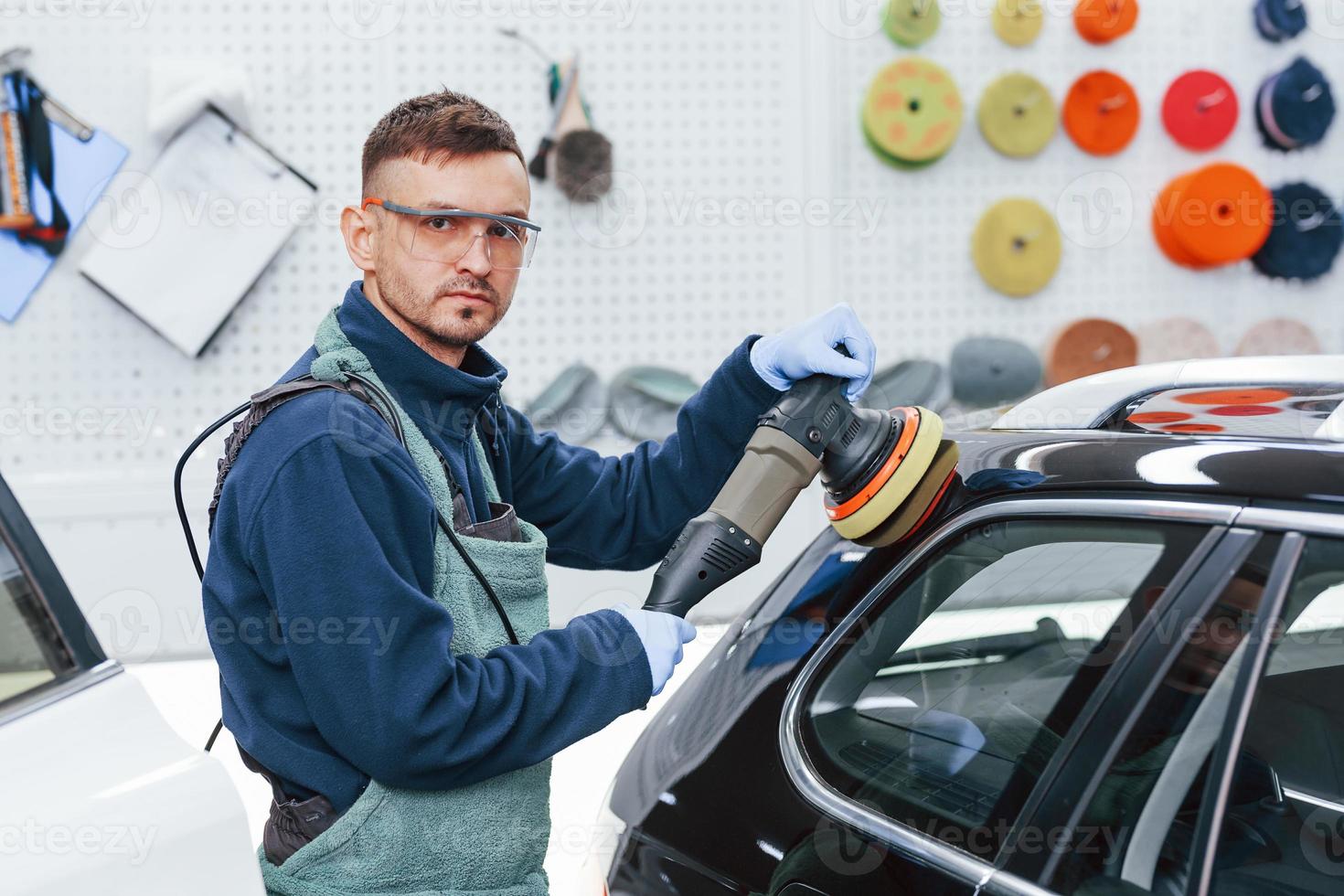 Male worker in uniform polishing new modern car. Conception of service photo