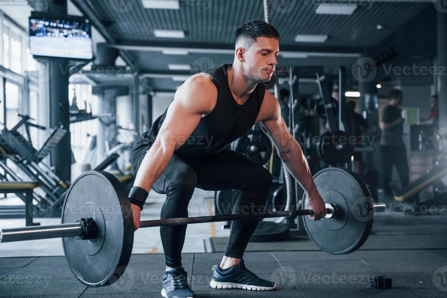 joven fuerte con ropa deportiva haciendo ejercicios con pesos pesados en el gimnasio foto