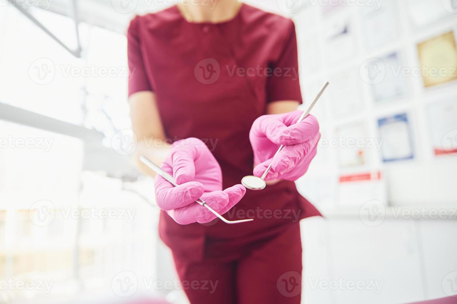 vista de cerca de una dentista en uniforme que está de pie en la oficina de estomatología con herramientas en las manos foto