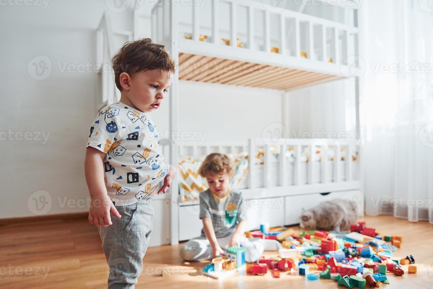 Two little boys have fun indoors in the bedroom with plastic construction set photo