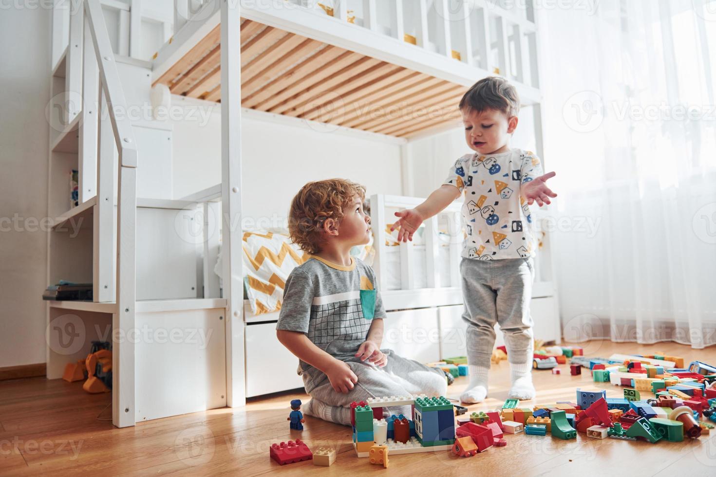 Two little boys have fun indoors in the bedroom with plastic construction set photo