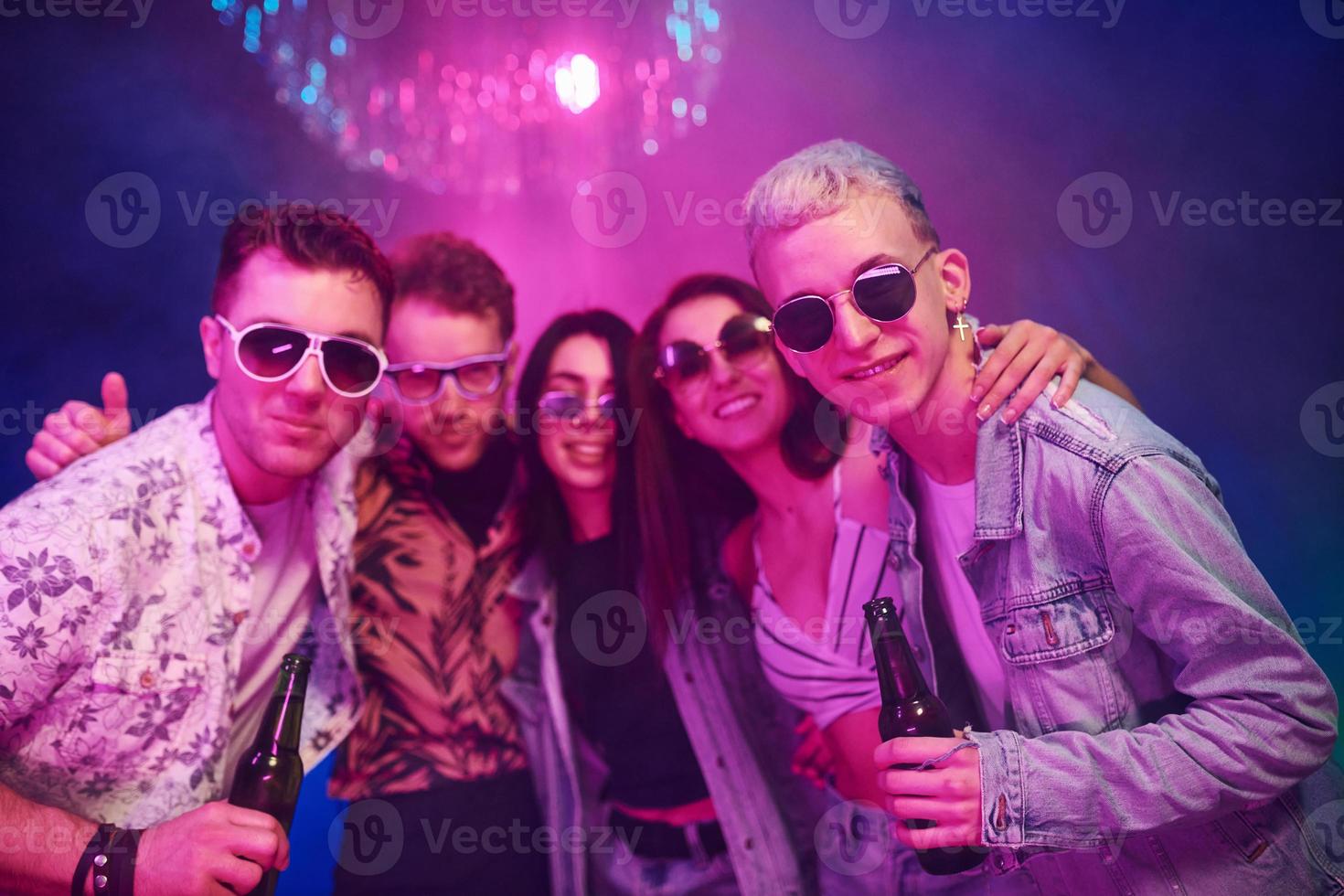 With bottles of beer in hands. Young people is having fun in night club with colorful laser lights photo