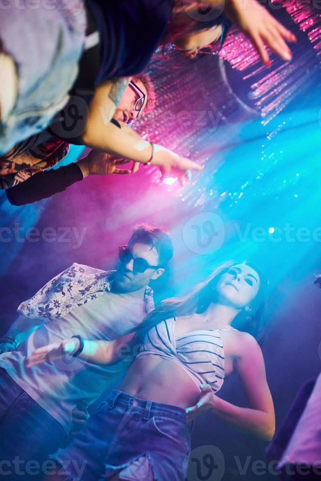 View from below of young people that having fun in night club with colorful laser lights photo