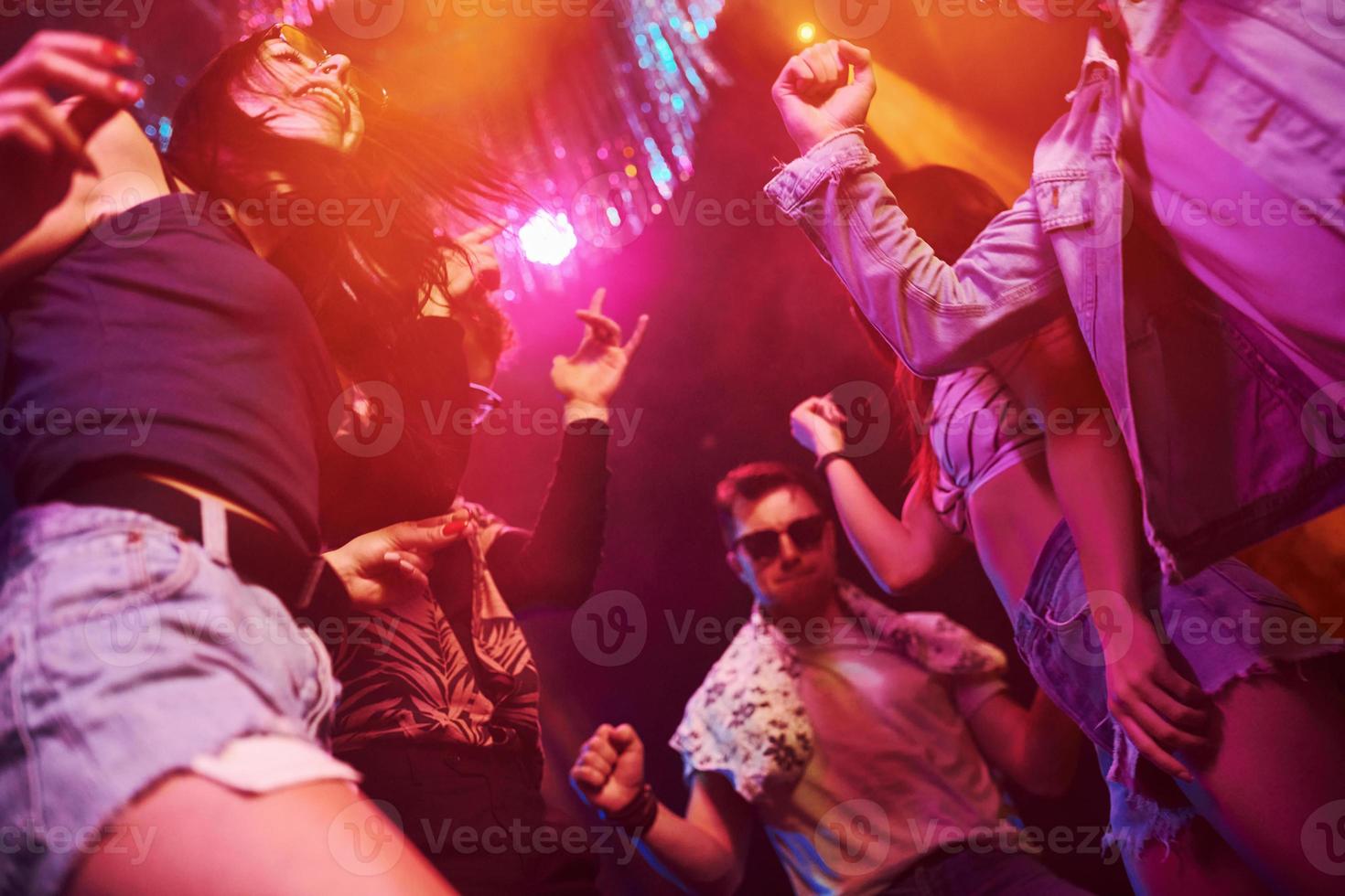 View from below of young people that having fun in night club with colorful laser lights photo