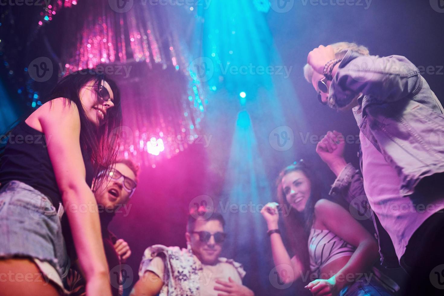 View from below of young people that having fun in night club with colorful laser lights photo