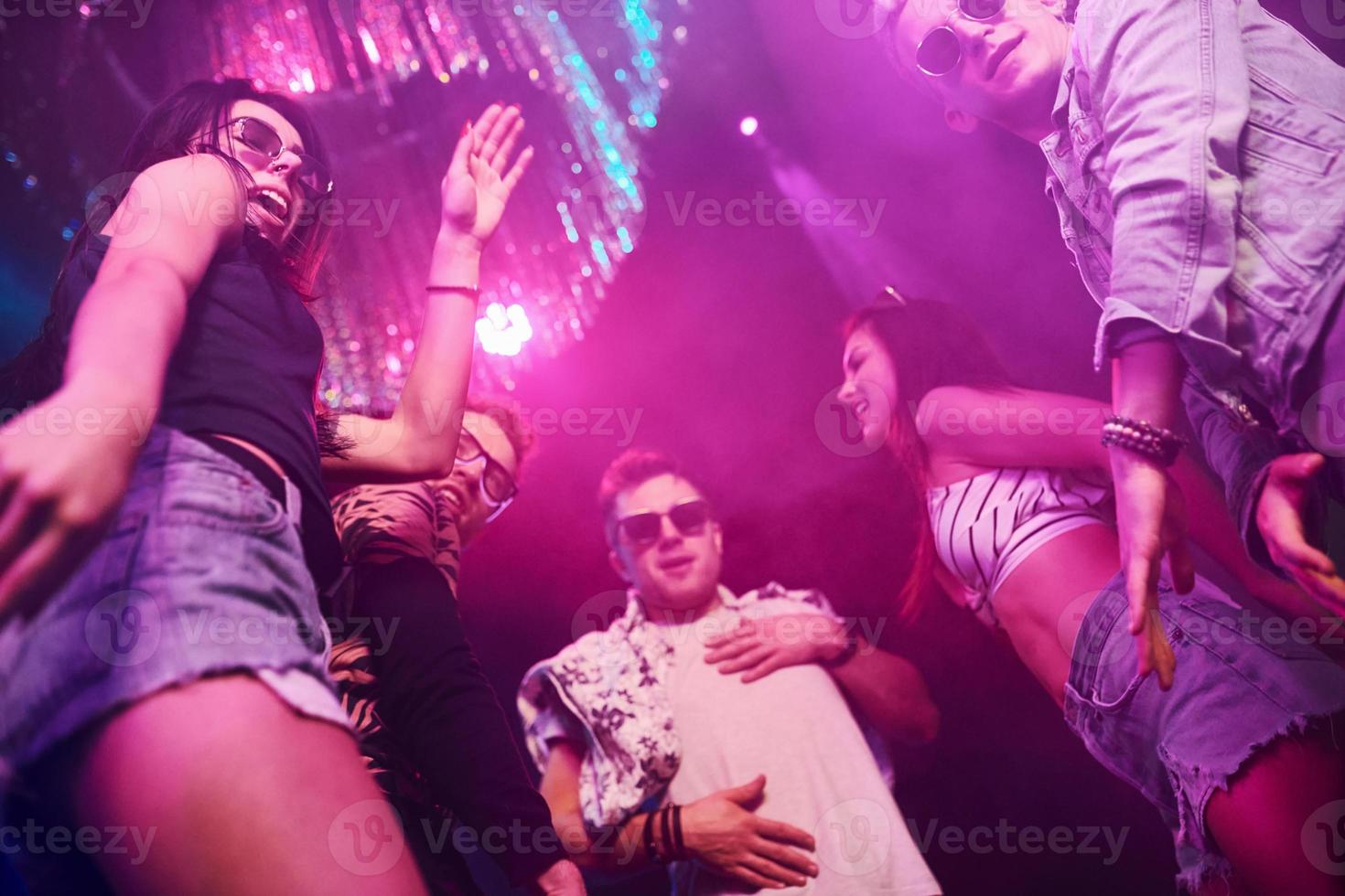 View from below of young people that having fun in night club with colorful laser lights photo