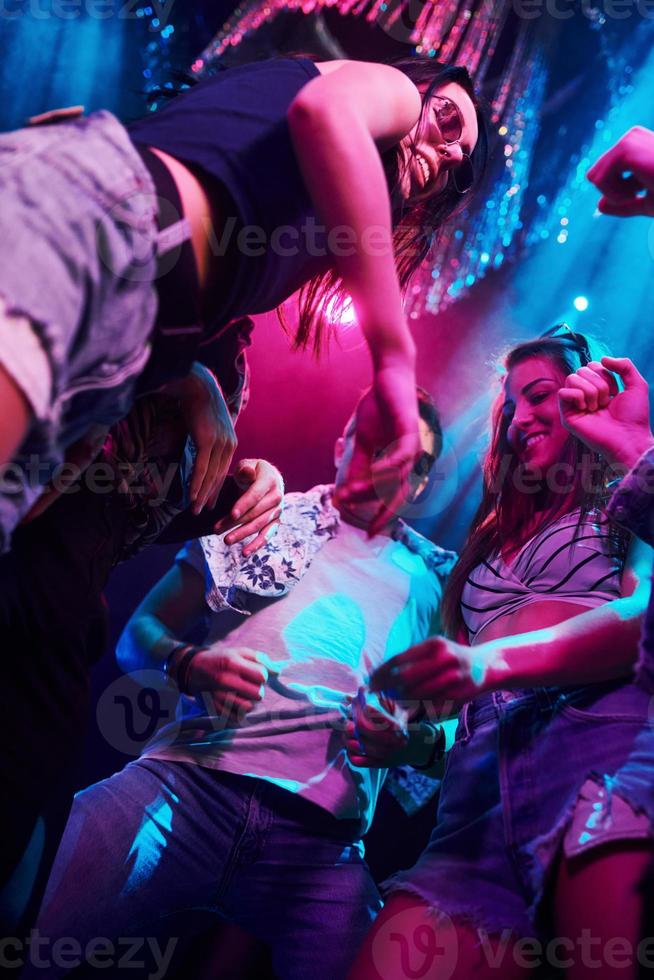 View from below of young people that having fun in night club with colorful laser lights photo