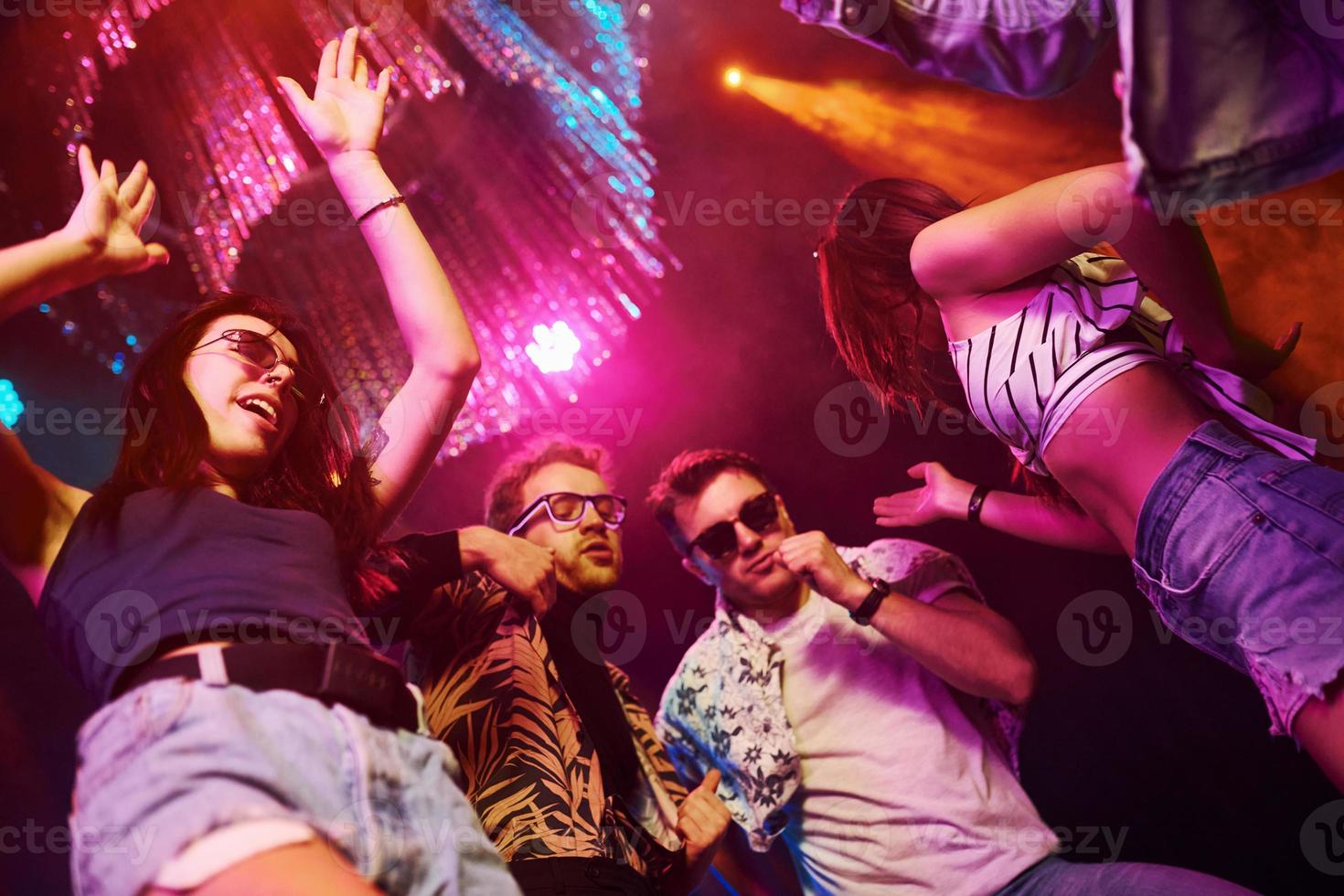 View from below of young people that having fun in night club with colorful laser lights photo