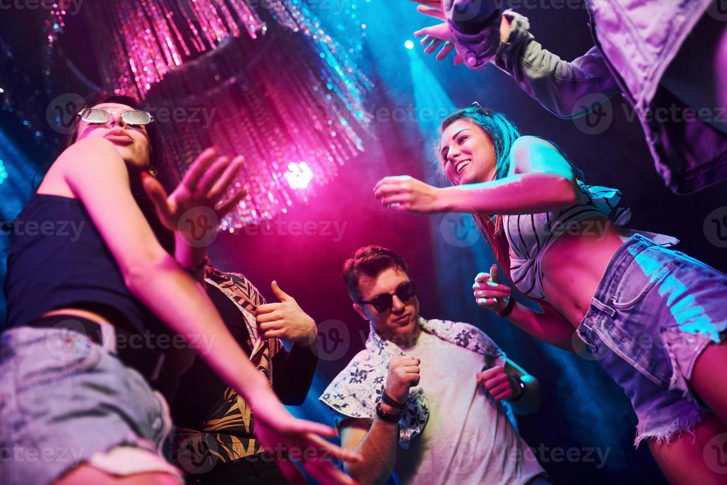 View from below of young people that having fun in night club with colorful laser lights photo