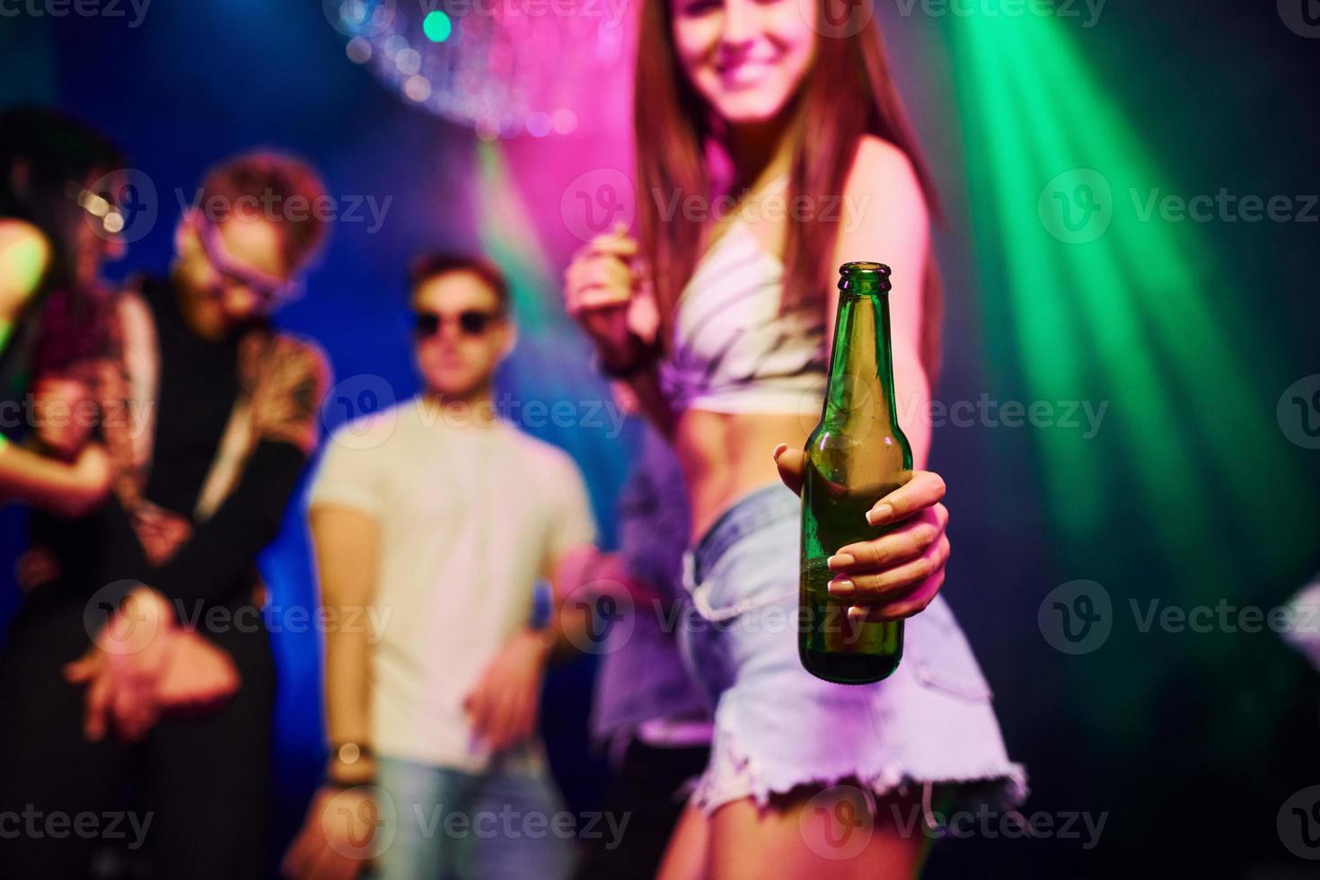 chica sosteniendo una botella. los jóvenes se divierten en el club nocturno con luces láser de colores foto