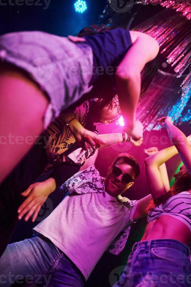 View from below of young people that having fun in night club with colorful laser lights photo