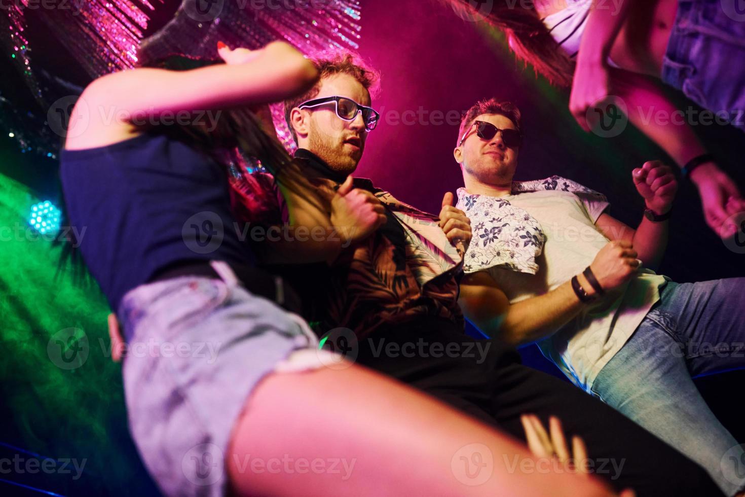 View from below of young people that having fun in night club with colorful laser lights photo