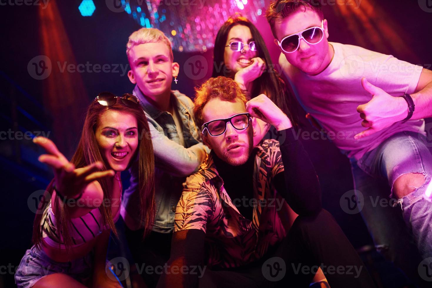 volviéndose locos y posando juntos para la cámara. los jóvenes se divierten en el club nocturno con luces láser de colores foto