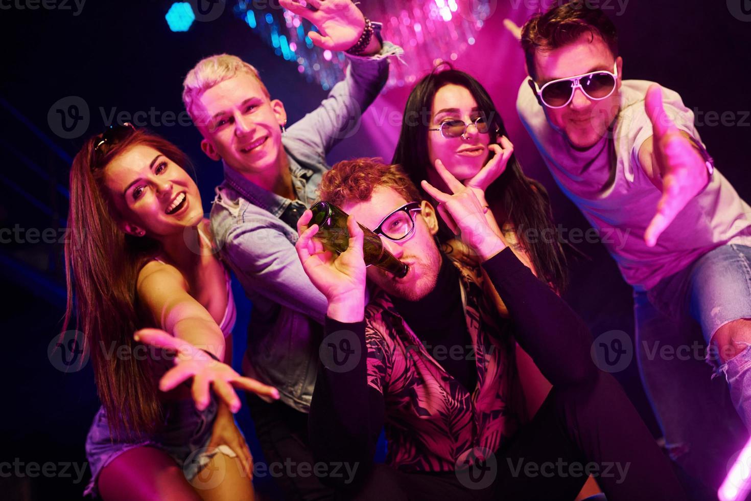 volviéndose locos y posando juntos para la cámara. los jóvenes se divierten en el club nocturno con luces láser de colores foto