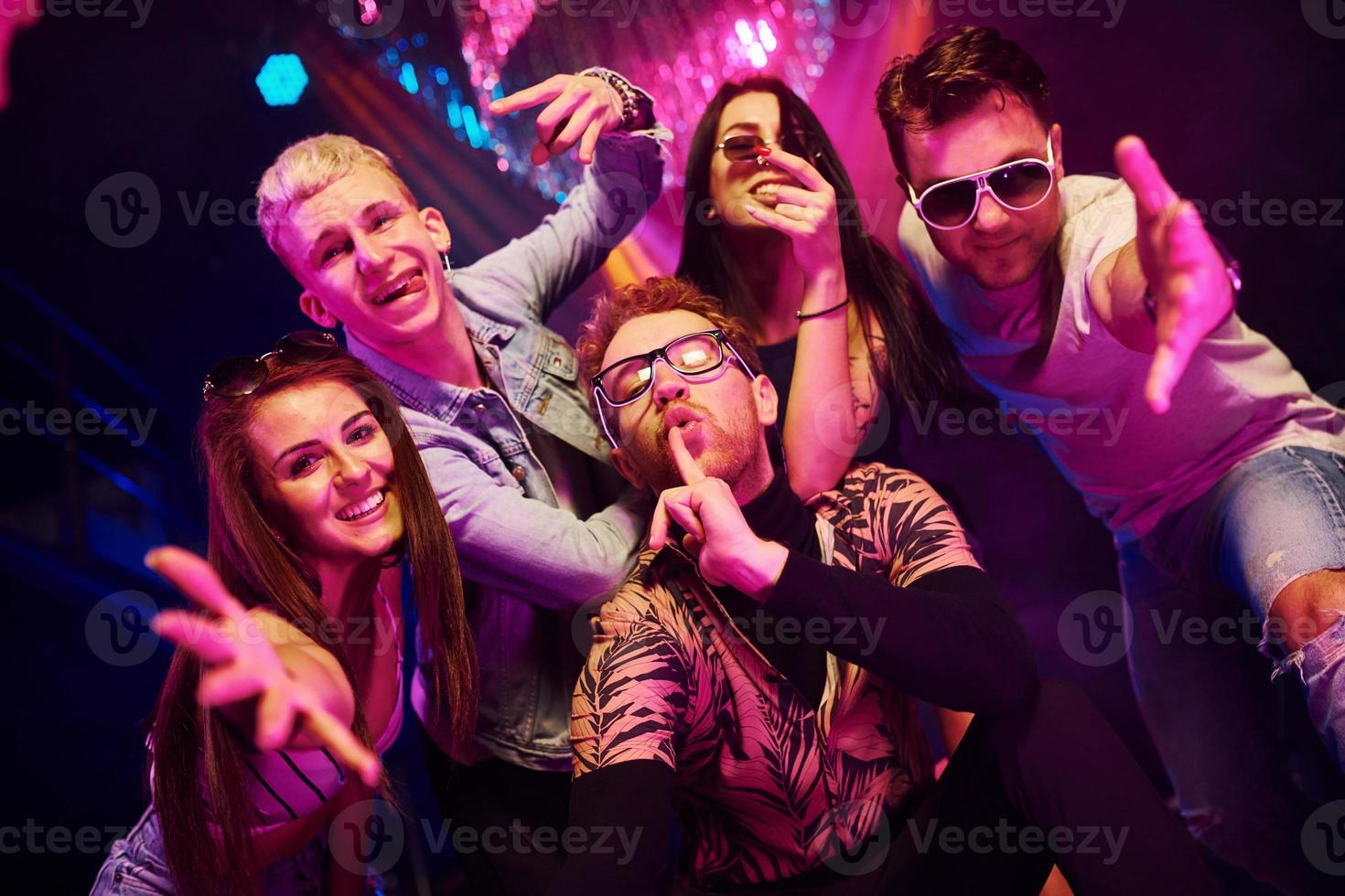 volviéndose locos y posando juntos para la cámara. los jóvenes se divierten en el club nocturno con luces láser de colores foto