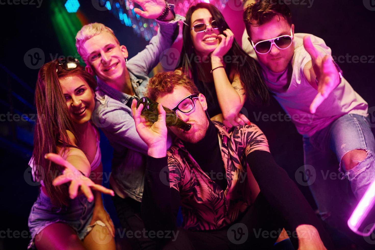 volviéndose locos y posando juntos para la cámara. los jóvenes se divierten en el club nocturno con luces láser de colores foto