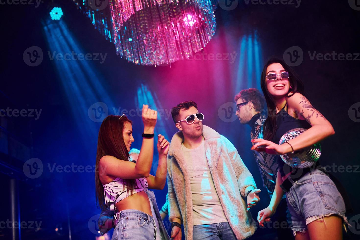 Elegant man in sunglasses in the midle feels like a boss. Young people is having fun in night club with colorful laser lights photo