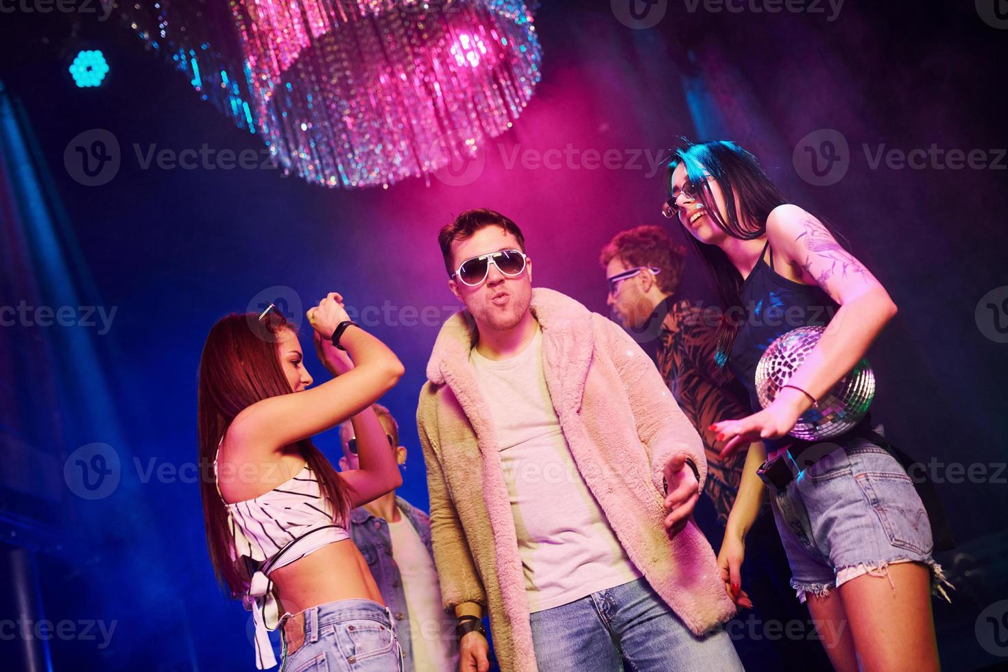 Elegant man in sunglasses in the midle feels like a boss. Young people is having fun in night club with colorful laser lights photo