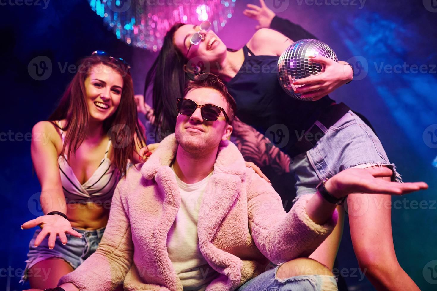 Elegant man in sunglasses in the midle feels like a boss. Young people is having fun in night club with colorful laser lights photo