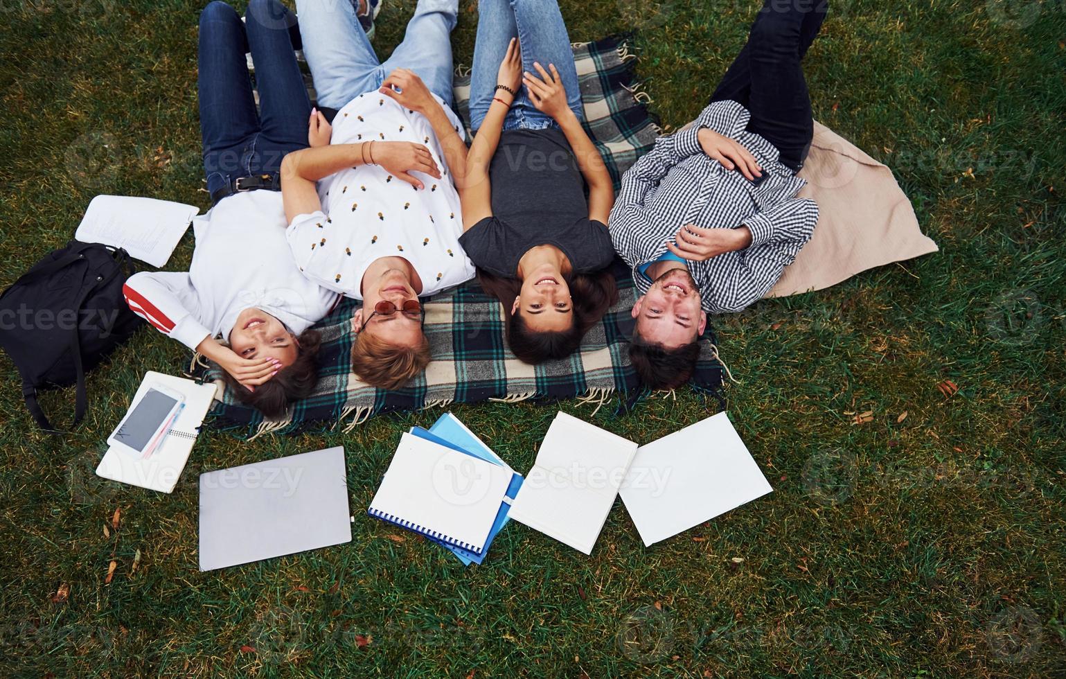 Having good rest. Group of young students in casual clothes on green grass at daytime photo