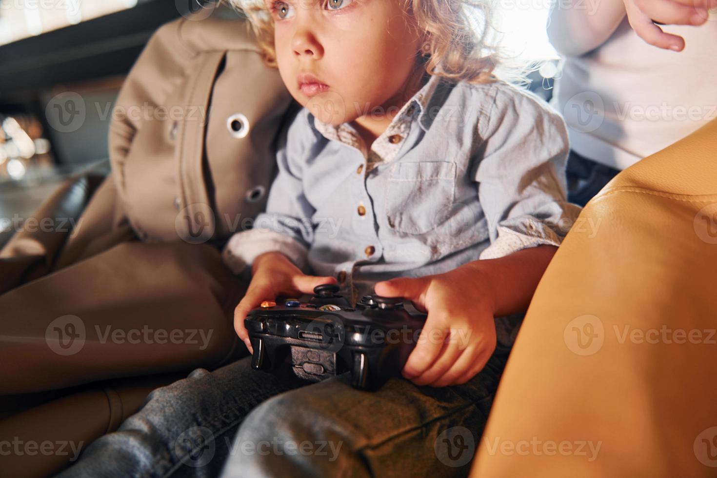 Kids in casual clothes sitting together with controller and playing video games photo