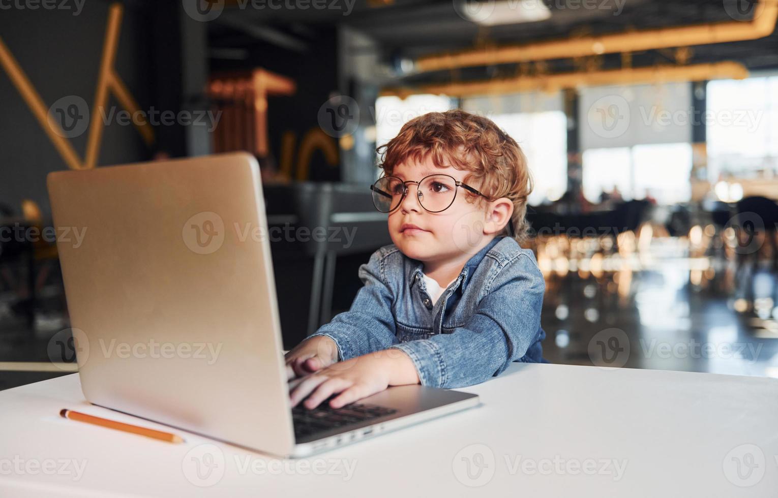 Smart child in casual clothes and in glasses using laptop for education purposes photo