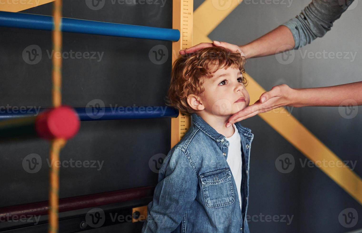 Teacher measuring kid's height indoors in kindergarten photo