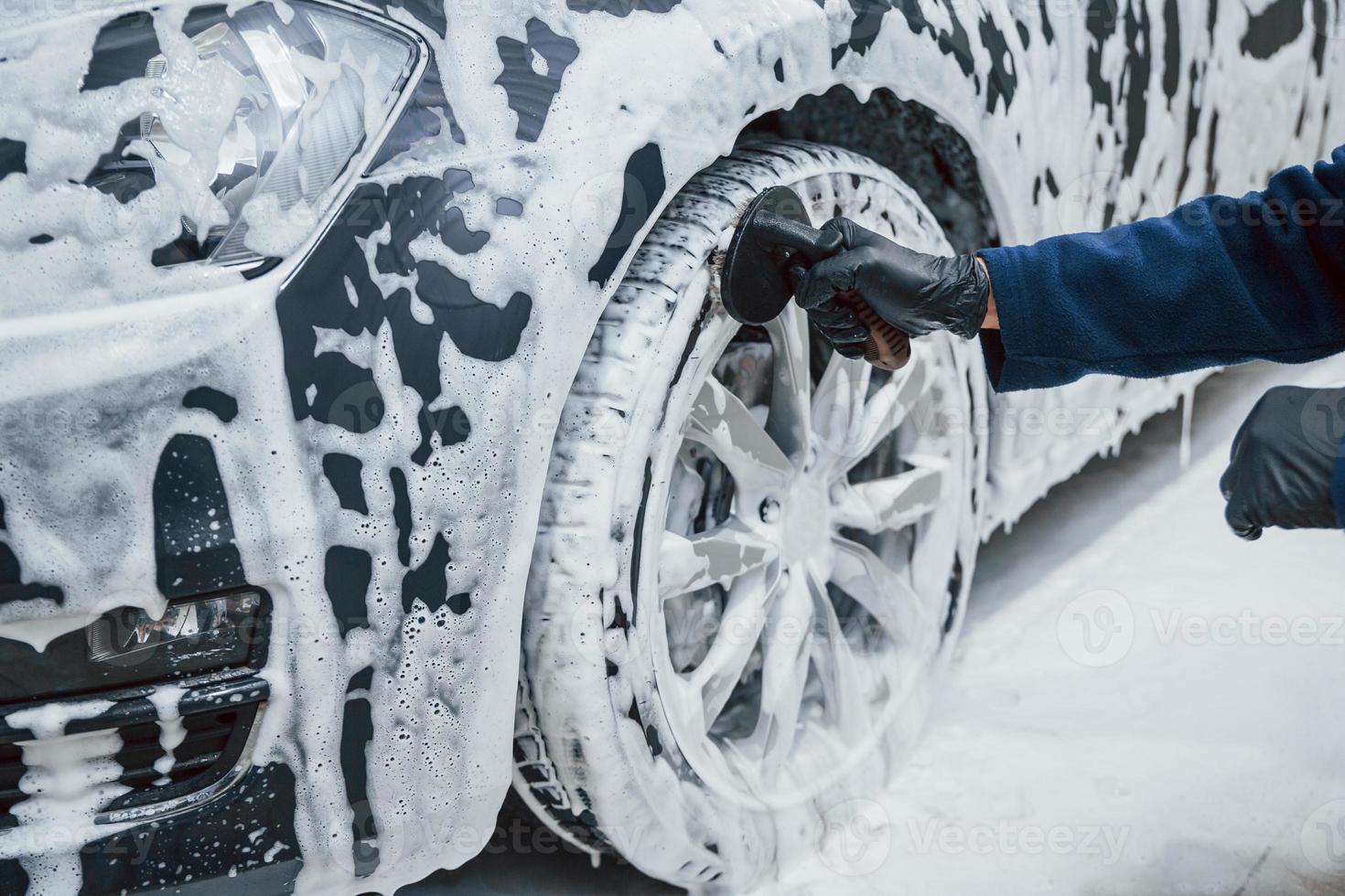 Male worker in uniform washing new modern car that covered with soap. Conception of service photo