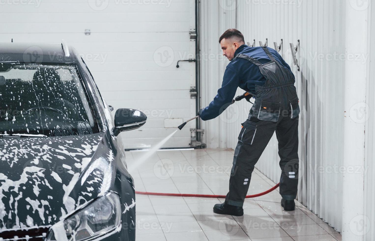 Male worker in uniform washing new modern car that covered with soap. Conception of service photo
