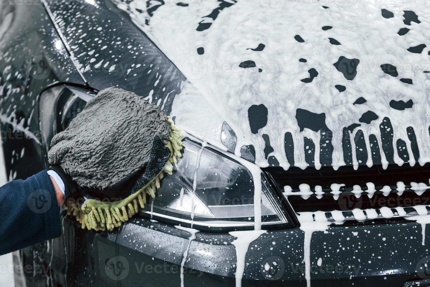 Male worker in uniform washing new modern car that is full of soap. Conception of service photo