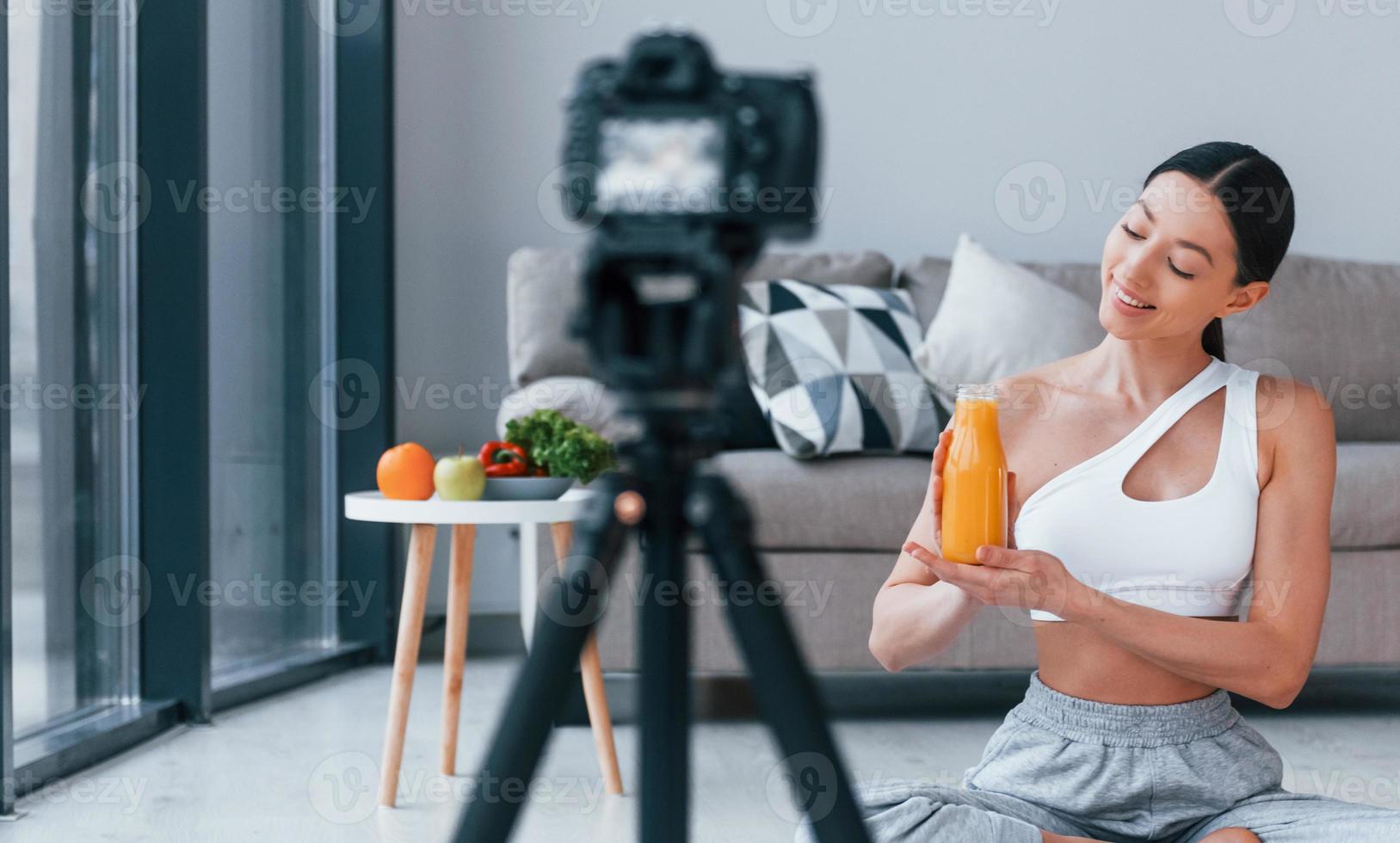 Blogger young woman with slim body shape in sportswear talking about vegetables, fruits and healthy food indoors at home photo