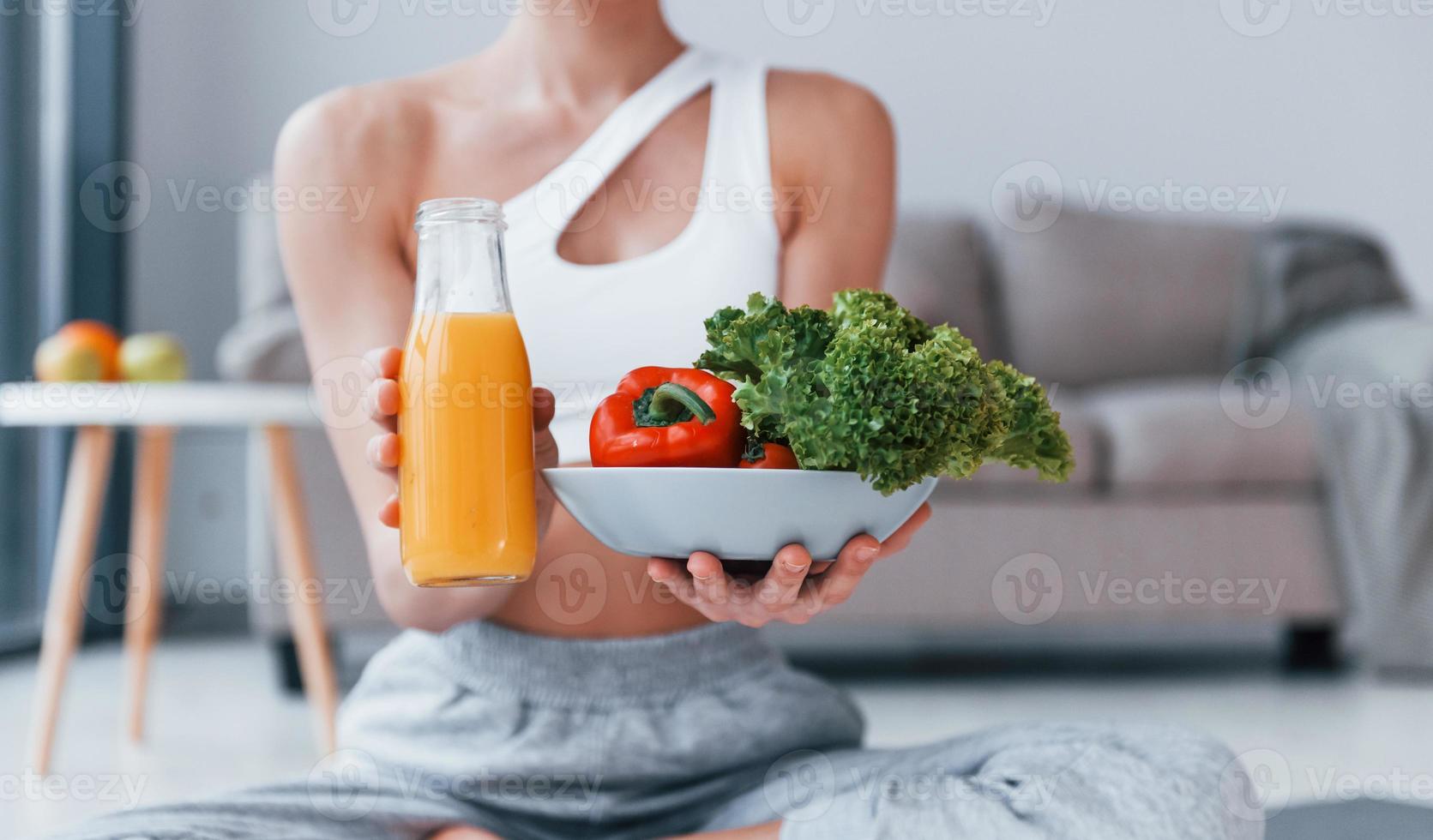 With healthy food and orange juice in hands. Young woman with slim body shape in sportswear have fitness day indoors at home photo