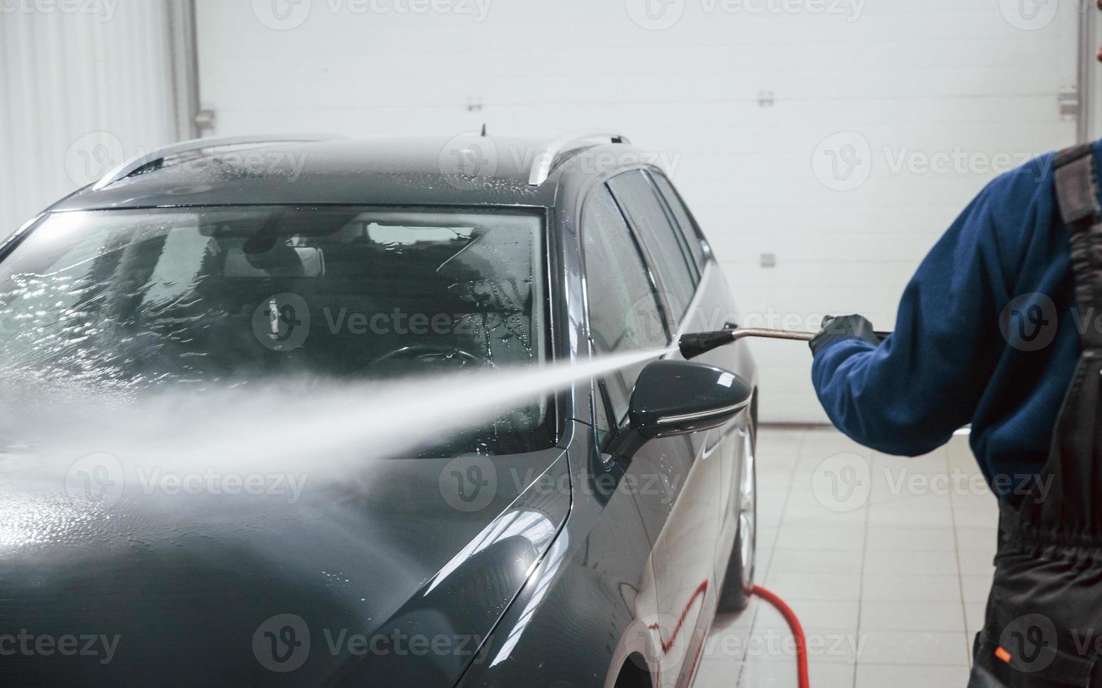 trabajador masculino en uniforme lavando auto nuevo y moderno en el interior. concepto de servicio foto