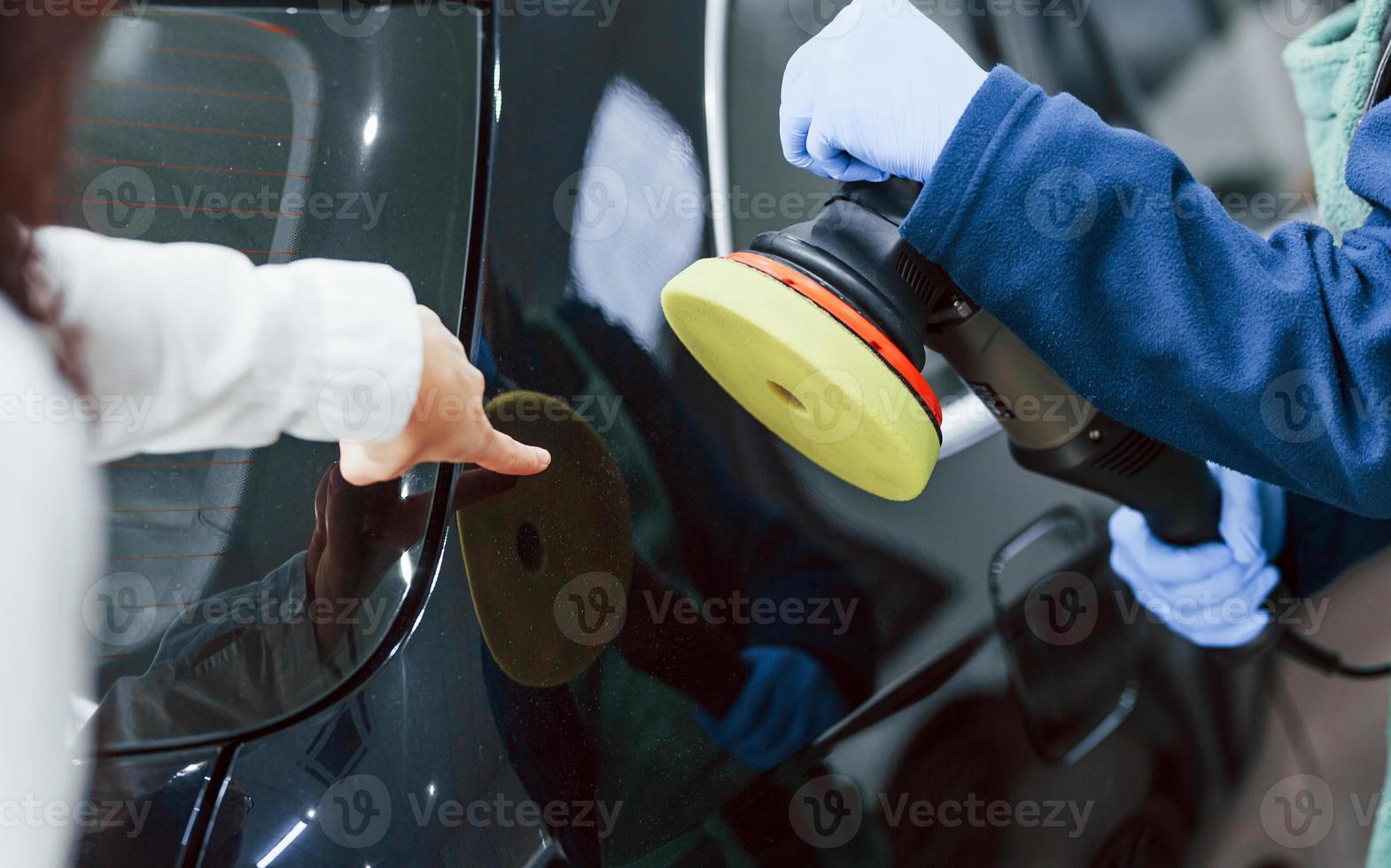 Female customer talking what to do. Male worker in uniform cleaning new modern car indoors. Conception of service photo