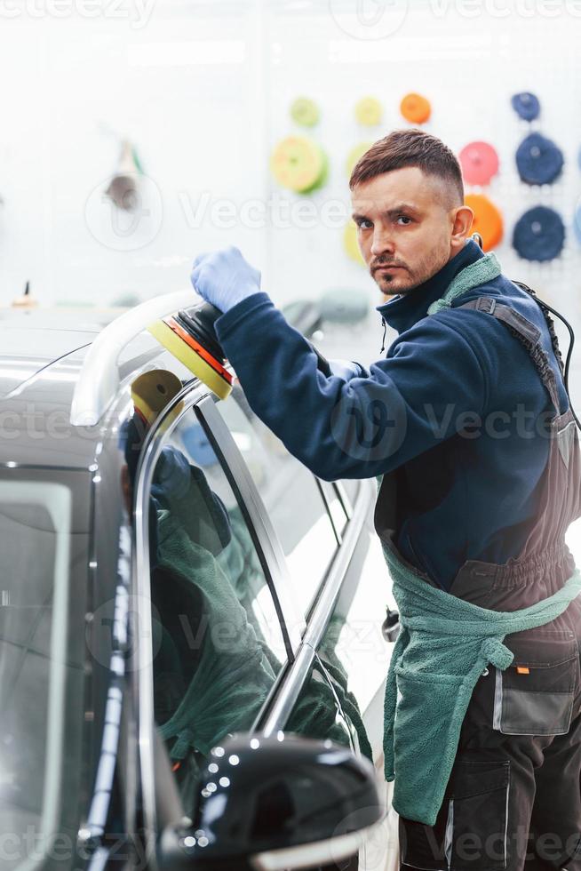 trabajador masculino en uniforme puliendo un coche nuevo y moderno. concepto de servicio foto
