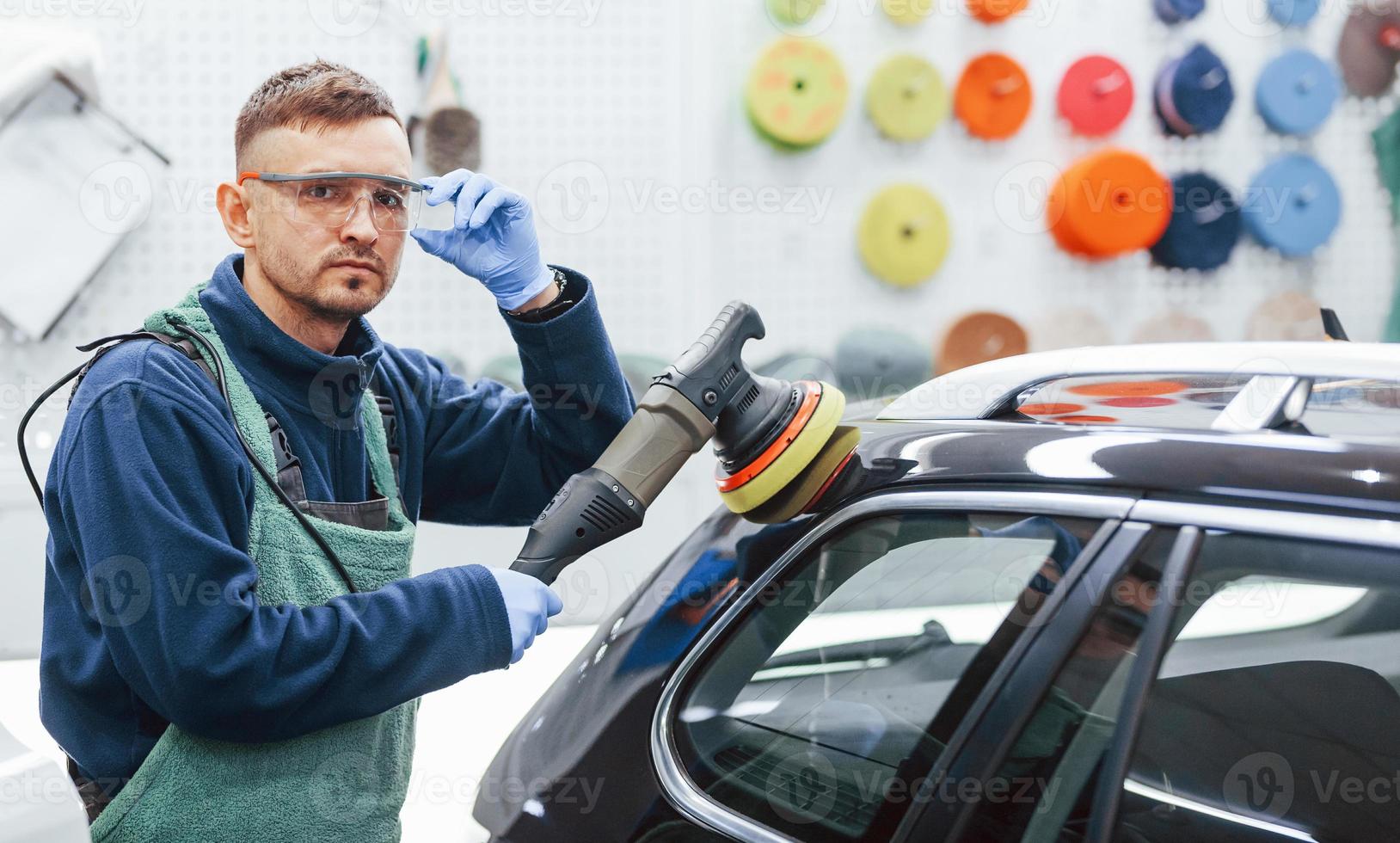 Male worker in uniform polishing new modern car. Conception of service photo