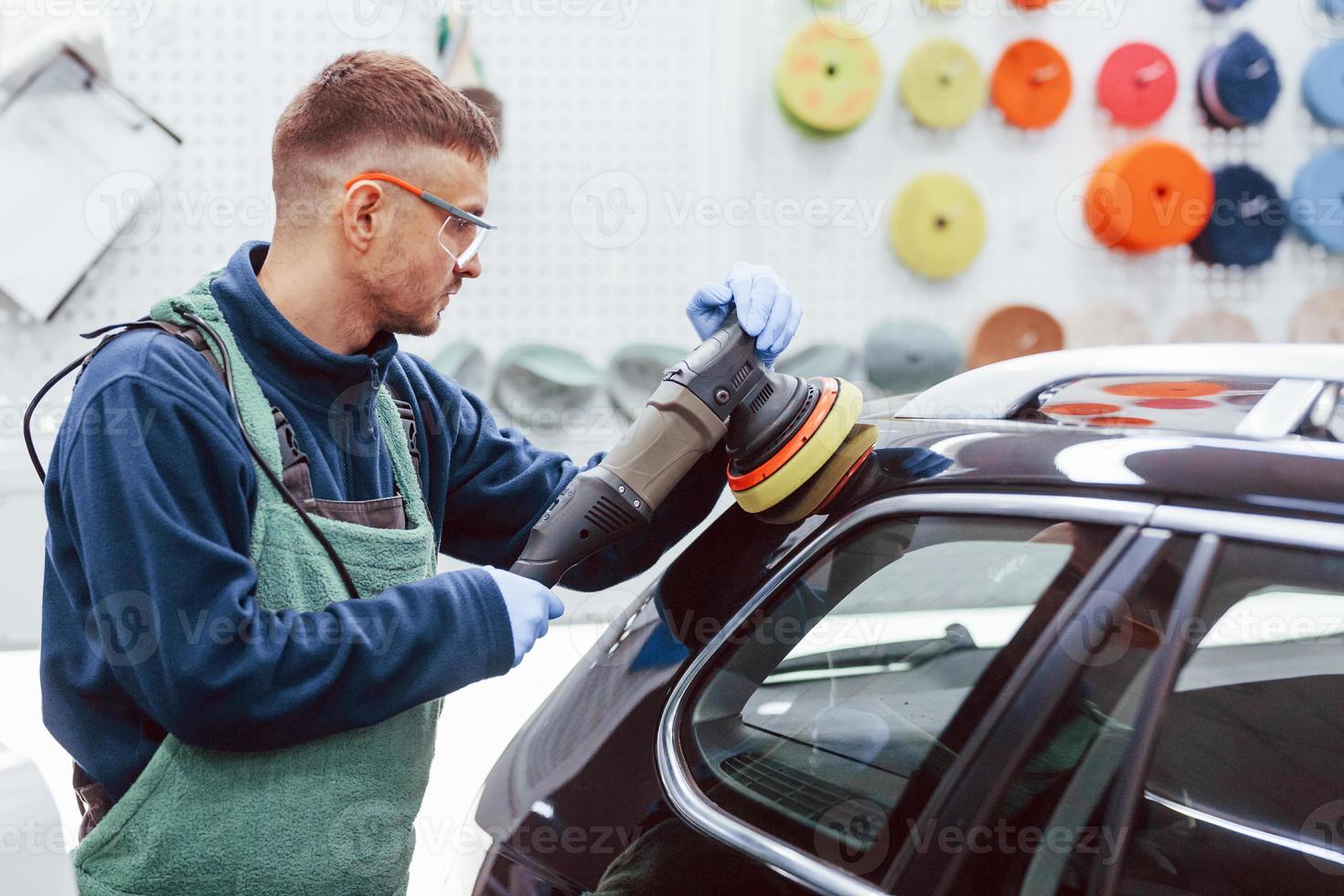 Male worker in uniform polishing new modern car. Conception of service photo