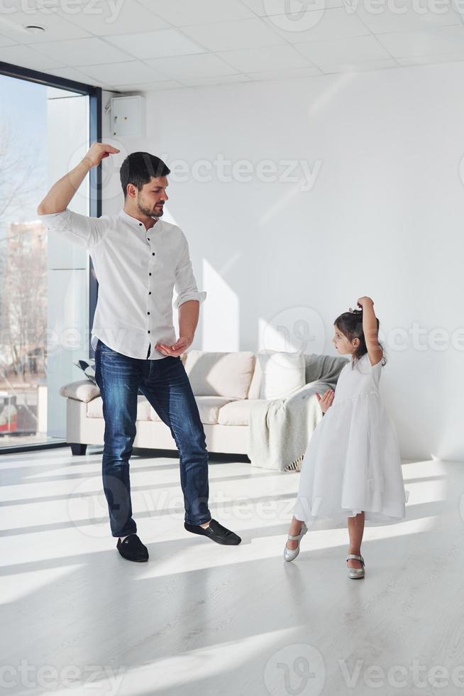 Happy father with his daughter in dress learning how to dance at home together photo