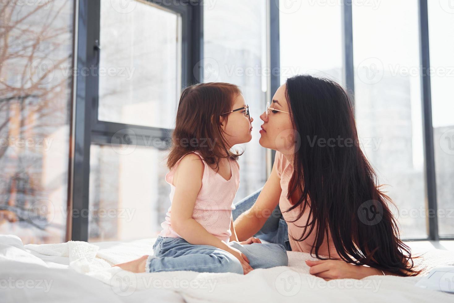 joven madre con su hija pasando el fin de semana juntos en la habitación y dando un beso foto