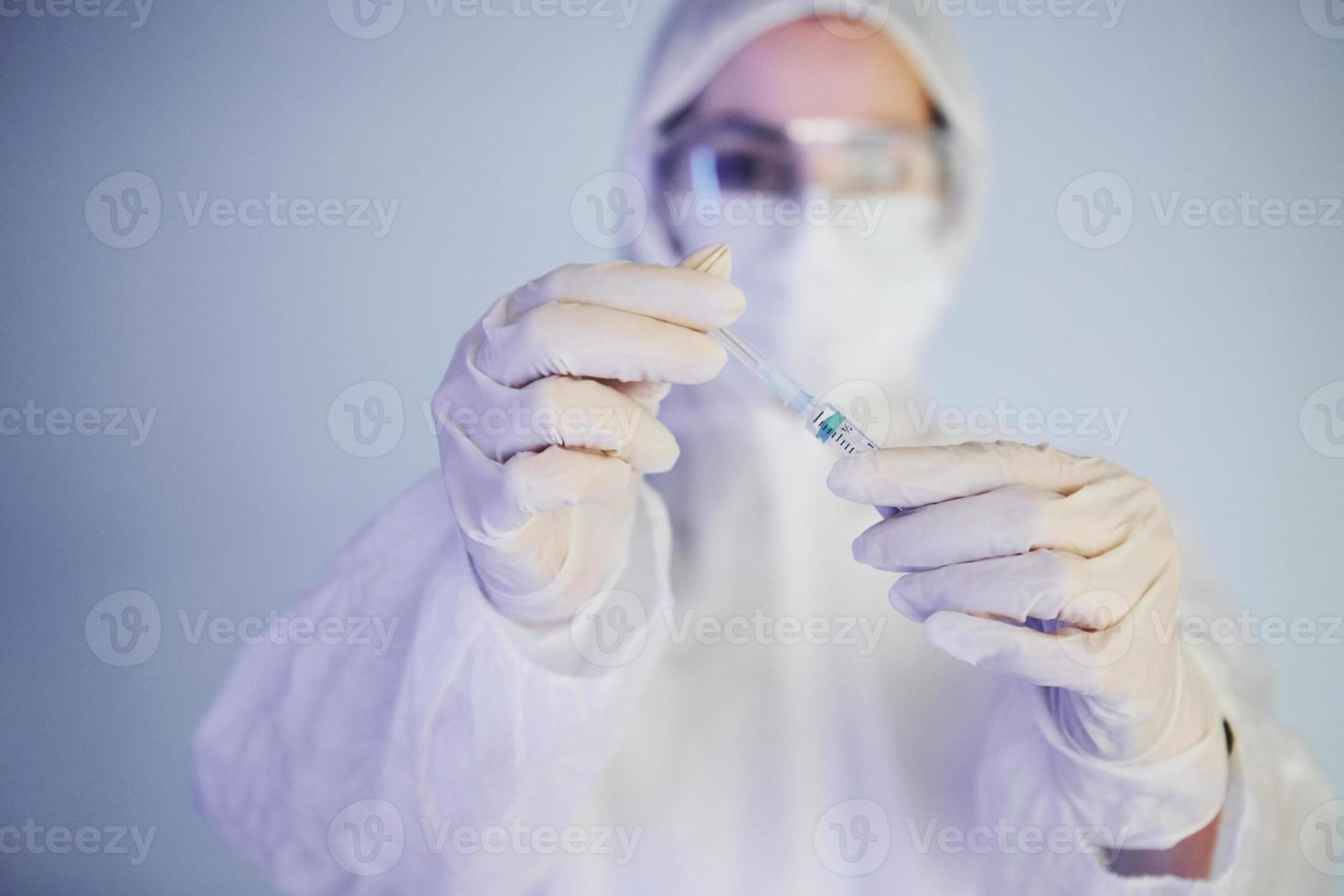 Holds syringe. Portrait of female doctor scientist in lab coat, defensive eyewear and mask photo