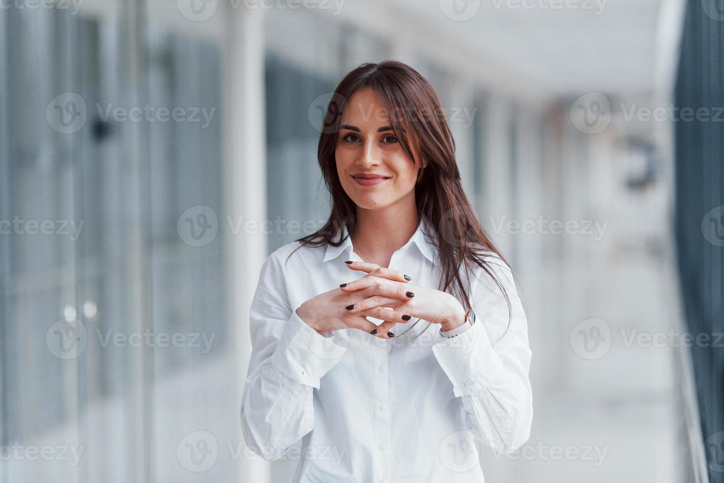 Brunette in white shirt that walks indoors in modern airport or hallway at daytime photo