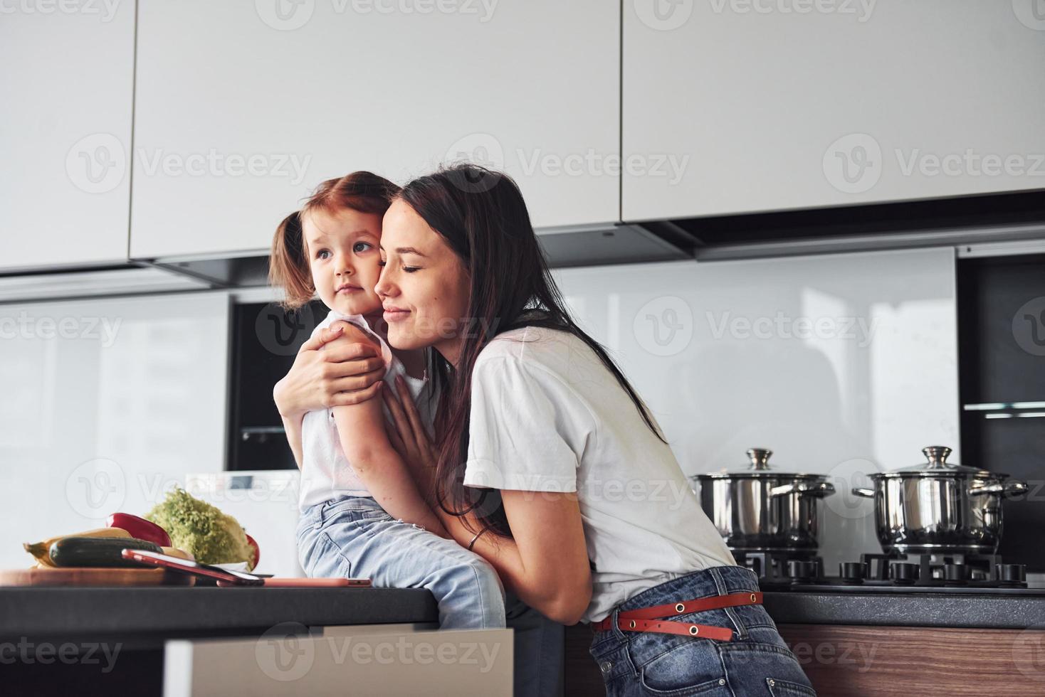 Mother with her little daughter embracing each other indoors in kitchen photo